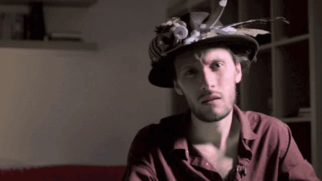 a man wearing a hat with feathers on it looks at the camera