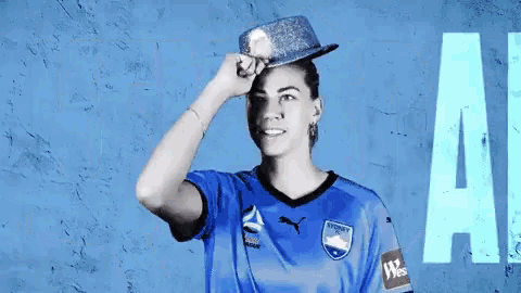 a woman wearing a sydney fc jersey holds a hat on her head