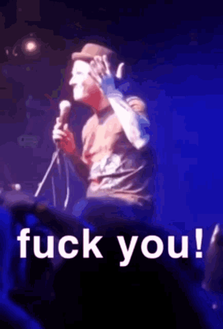 a man singing into a microphone with the words " fuck you " behind him