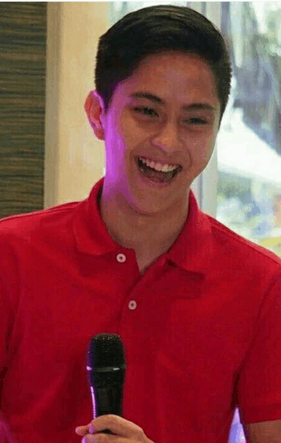 a man in a red shirt is holding a microphone and laughing