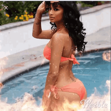 a woman in a bikini is standing next to a swimming pool surrounded by flames .