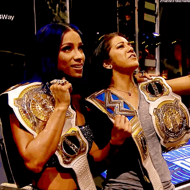 two female wrestlers are posing for a photo with their championship belts on their shoulders