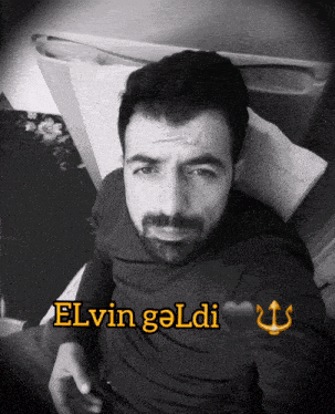 a man with a beard is laying on a bed with the words elvin goldi written on his chest