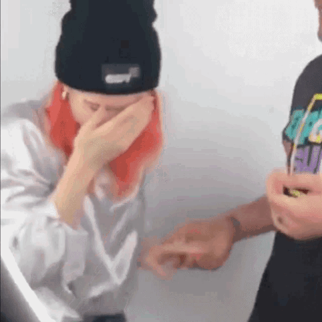 a woman with red hair is covering her face with her hands while a man holds her hand .