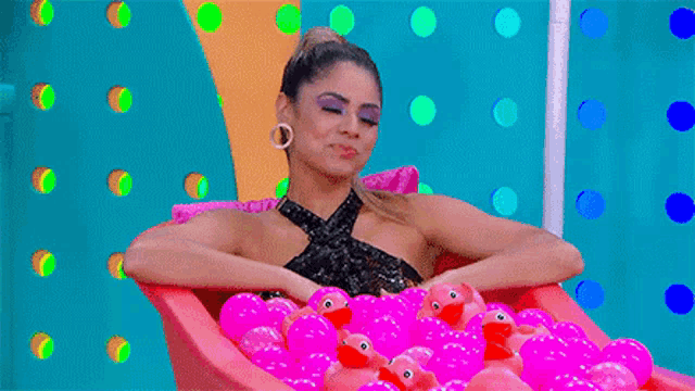 a woman is taking a bath in a tub filled with pink rubber ducks .