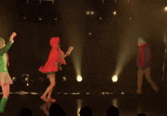 a group of people are dancing on a stage in front of a purple light