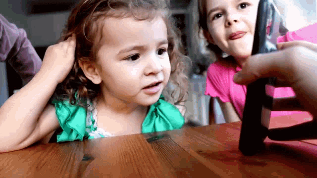 two little girls are sitting at a table looking at a phone
