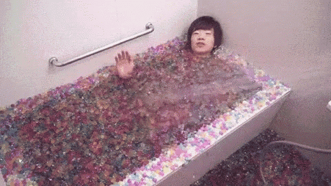 a person is laying in a bathtub filled with lots of colorful beads .