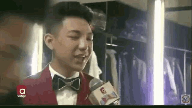 a young man in a tuxedo and bow tie is talking into a microphone .