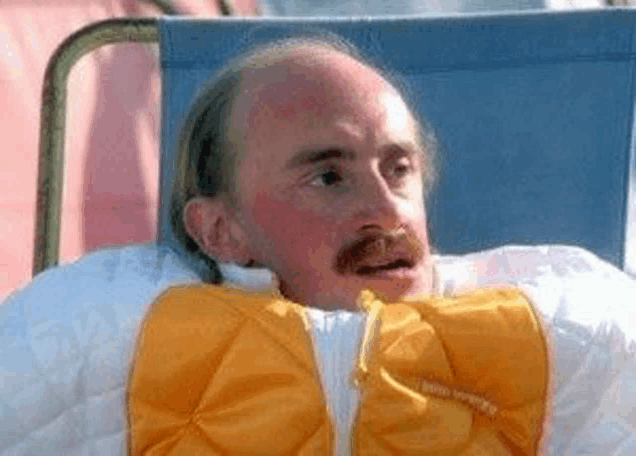 a bald man with a mustache is laying in a chair with a yellow jacket on .