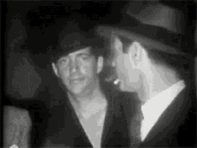 a man in a hat is smoking a cigarette while another man looks on