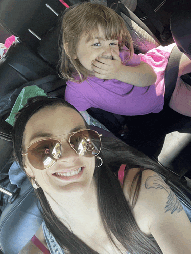 a woman wearing sunglasses is sitting next to a little girl who is covering her mouth