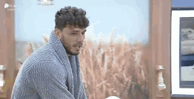 a man with curly hair and a beard is wearing a blue sweater and a blue towel around his neck .
