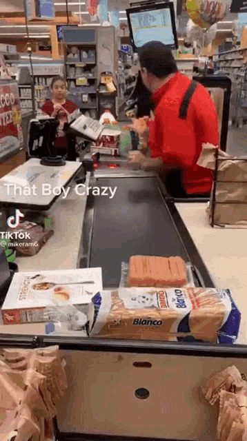 a man in a red shirt is standing behind a counter in a grocery store .
