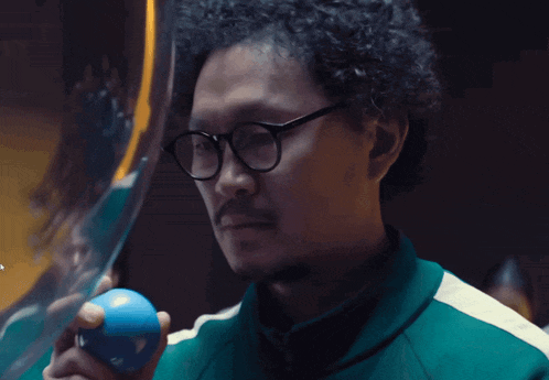 a man with glasses holds a blue ball in his hand