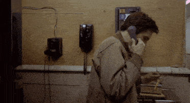 a man talking on a pay phone with a sticker on the wall that says ' a '