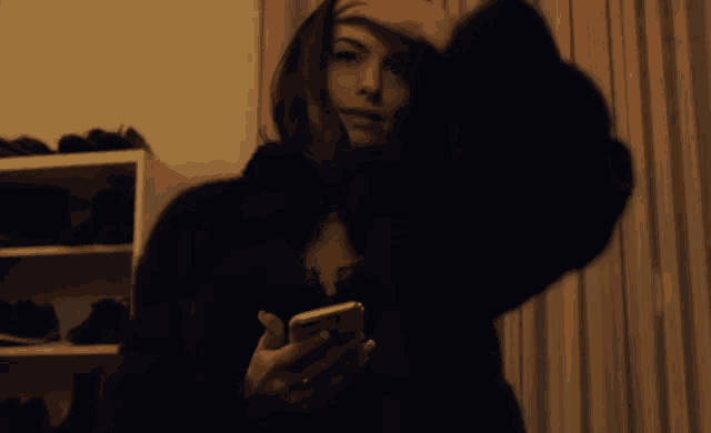 a woman in a black fur coat is holding a cell phone