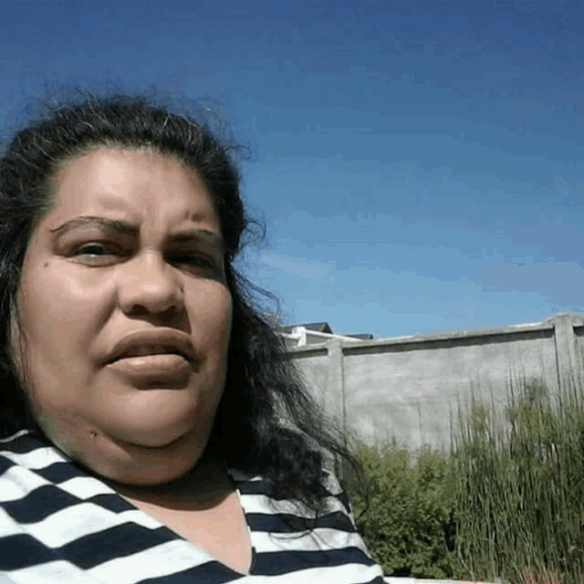 a woman in a striped shirt looks at the camera with a fence in the background