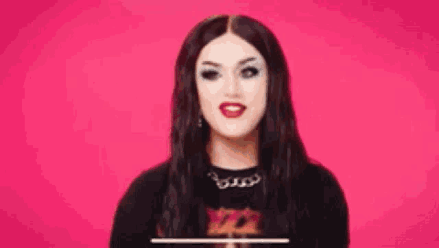 a woman with long black hair and red lips is wearing a black shirt and necklace .
