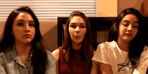 three young women are sitting next to each other in a room and looking at the camera .