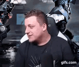 a man in a black shirt is sitting in a chair with a robot in the background .