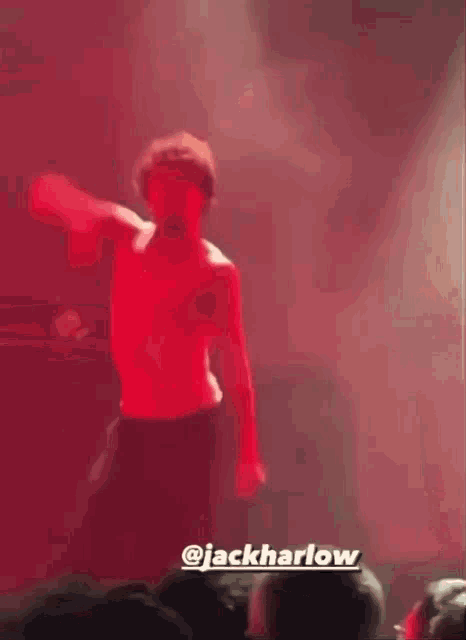 a man in a red shirt is standing on a stage in front of a crowd with the name jackharlow on the bottom right corner