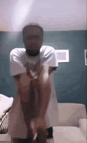 a man in a white shirt is standing on a couch .