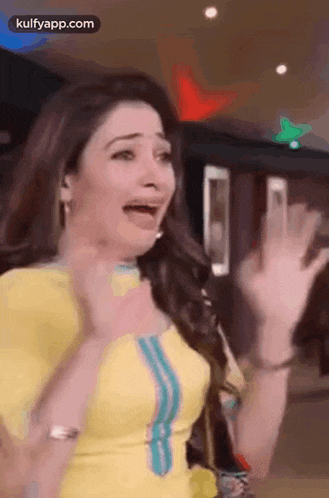 a woman in a yellow dress is making a funny face while waving her hands .