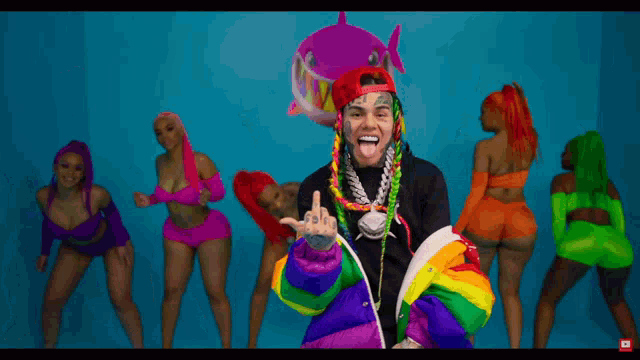 a group of women are dancing in front of a man with a rainbow jacket on
