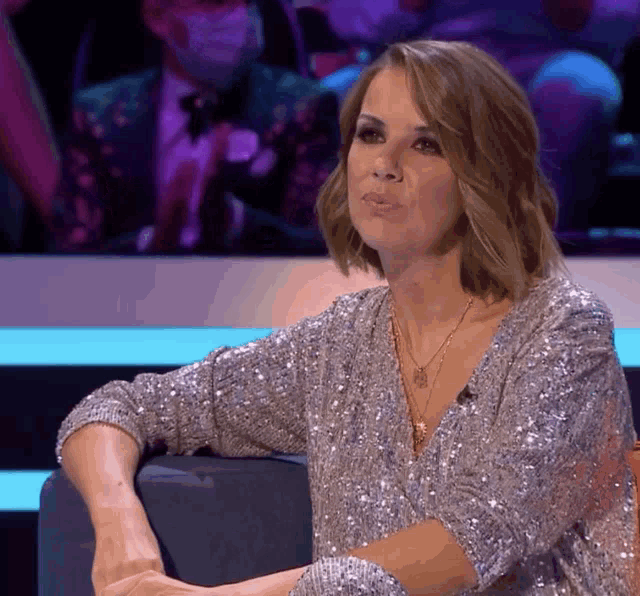 a woman wearing a sequined top is sitting on a couch