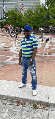 a man standing in front of a fountain wearing a blue hat and sunglasses