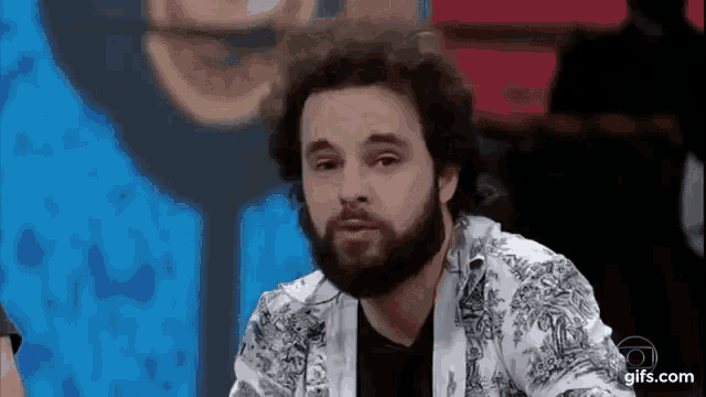 a man with a beard is sitting at a table and making a face .