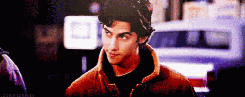 a young man in a brown jacket is standing in front of a car .