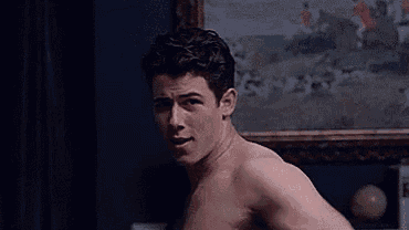 a shirtless man is sitting in front of a painting and looking at the camera .