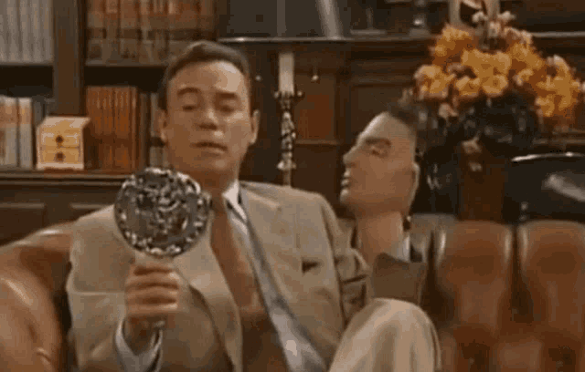 a man in a suit and tie is sitting on a couch holding a mirror ..