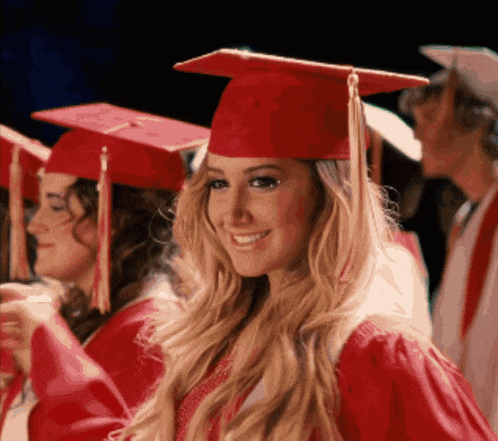 a woman wearing a red graduation cap and gown smiles for the camera