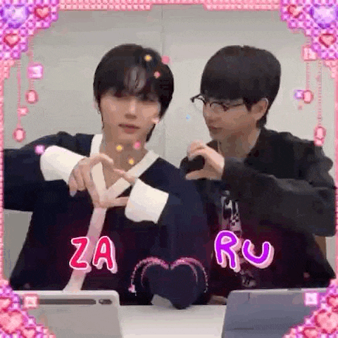 two men are making a heart shape with their hands while sitting at a table with laptops .