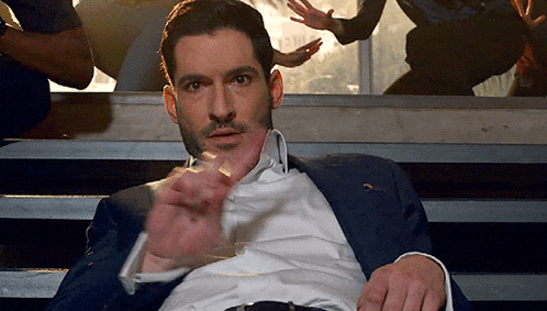 a man in a suit and white shirt is sitting on a set of stairs and pointing at something .