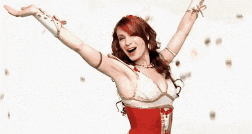 a woman in a red and white dress is standing with her arms outstretched and confetti is falling around her .