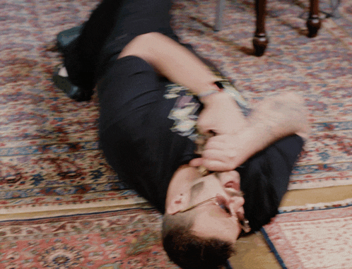 a man in a black shirt is laying on the floor playing a violin