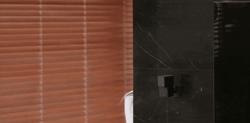 a woman is peeking out from behind a glass door in a bathroom .
