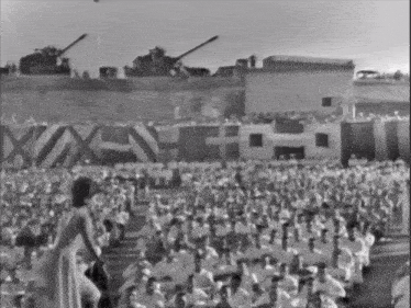 a woman stands in front of a crowd of people with a sign that says " x " on it
