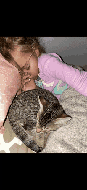 a little girl in a purple shirt kisses a cat on the nose