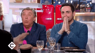two men are sitting at a table with glasses of wine and the number 5 on the screen