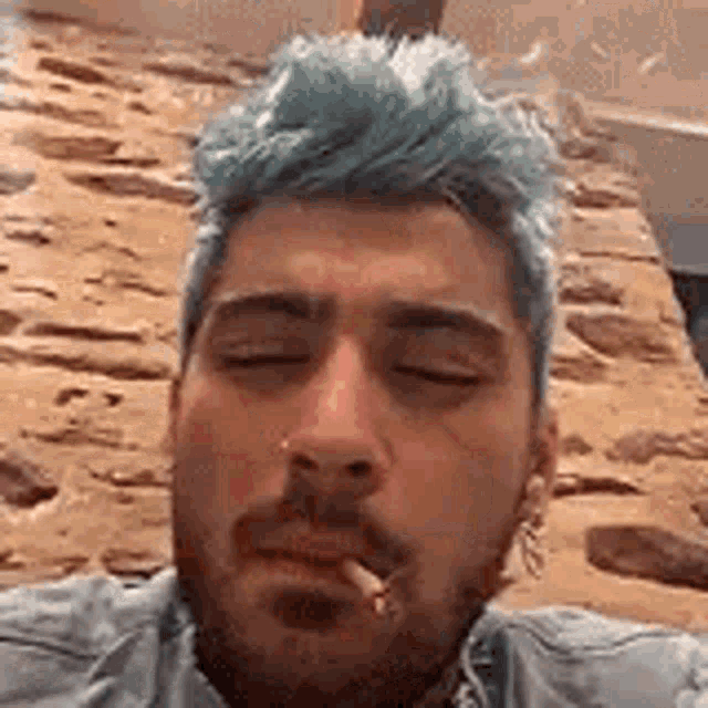 a man with blue hair is smoking a cigarette and taking a selfie .