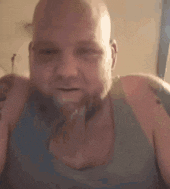 a bald man with a beard is wearing a tank top and has tattoos on his shoulder .