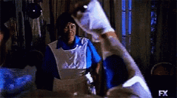 a woman in an apron is standing next to a man in a blue shirt in a room .