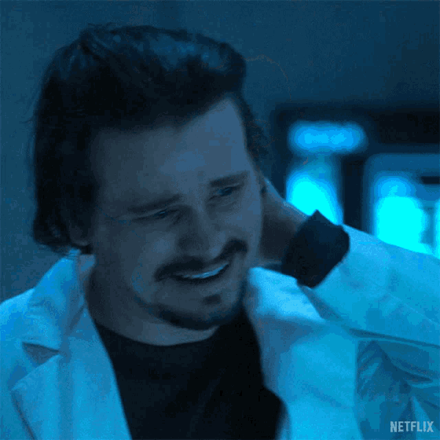 a man with a beard is wearing a lab coat and smiling while holding his neck .