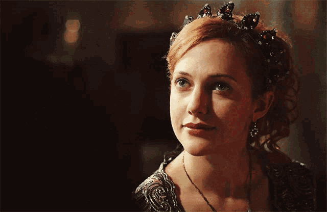 a woman wearing a tiara and a necklace looks at the camera