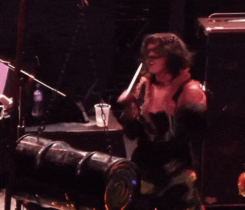 a woman singing into a microphone while standing in front of a drum